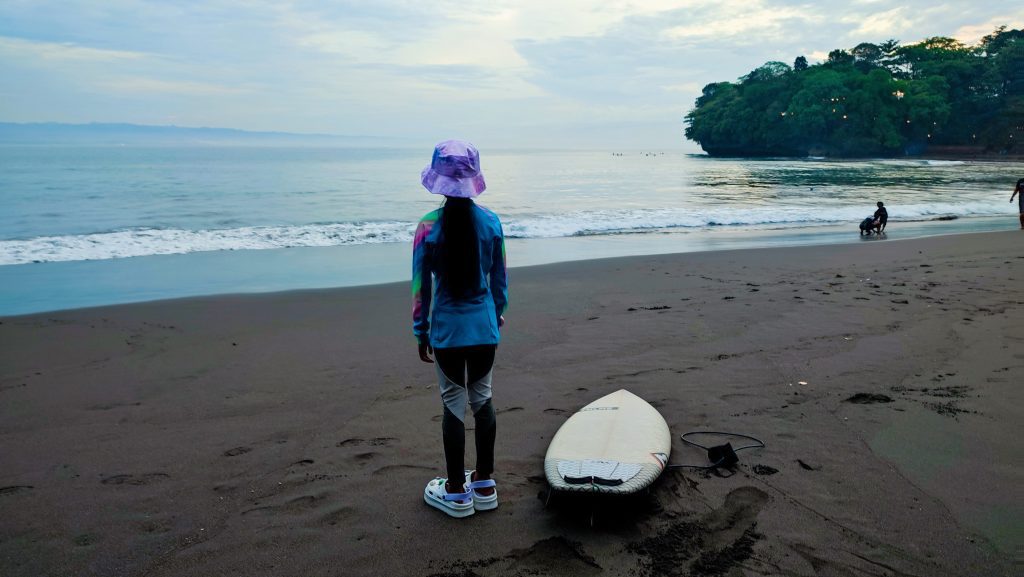 Intan, an 8-year-old surfer girl from Batukaras, standing on the beach in the morning